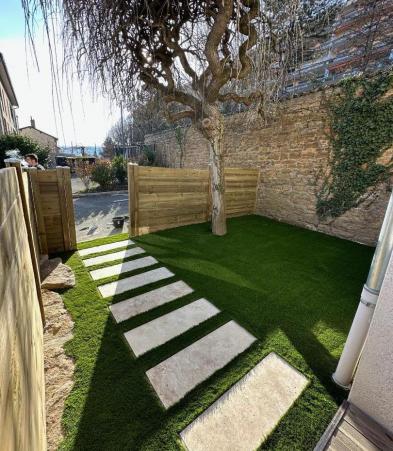 Création d'un jardin, palissade en bois, gazon synthétique et dalles en travertin pour l'allée